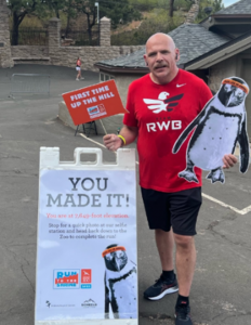 Photo of Duane holding "You made it" signs at the end of his 10-mile race